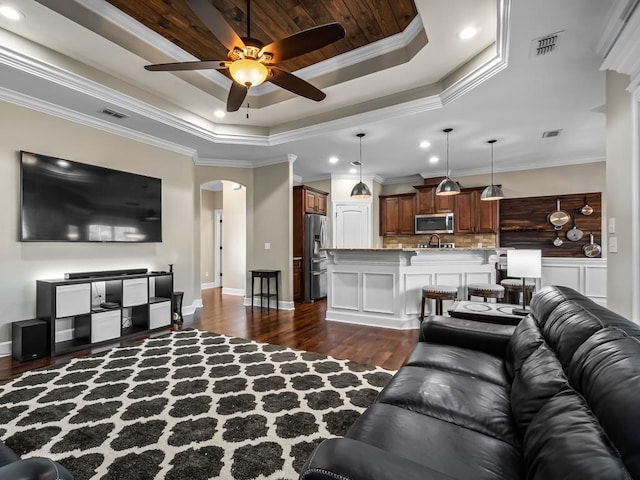 living room with dark hardwood / wood-style flooring, a tray ceiling, ceiling fan, crown molding, and sink