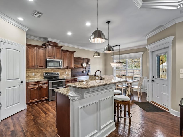 kitchen with pendant lighting, a breakfast bar area, an island with sink, light stone counters, and stainless steel appliances