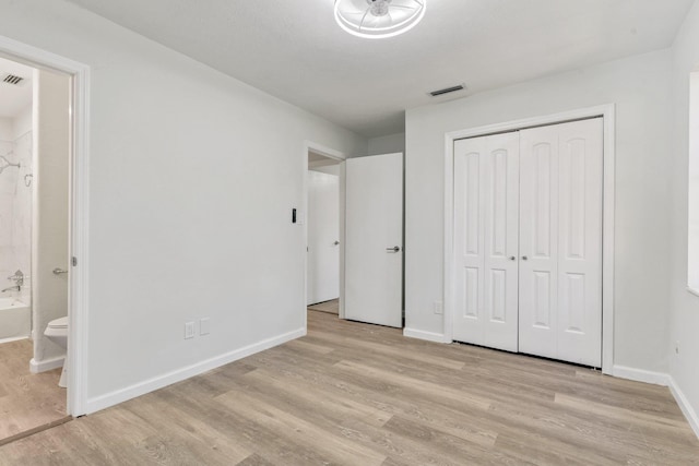 unfurnished bedroom with connected bathroom, light wood-type flooring, and a closet