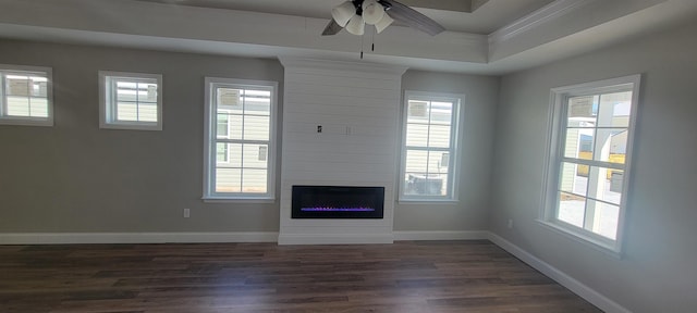 unfurnished living room with dark hardwood / wood-style floors, a large fireplace, ceiling fan, and a tray ceiling