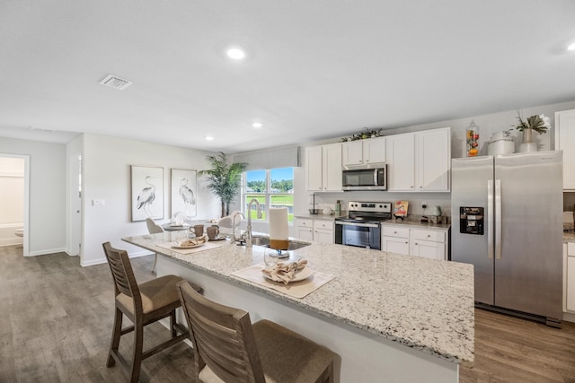 kitchen featuring a center island with sink, appliances with stainless steel finishes, a kitchen bar, light hardwood / wood-style floors, and white cabinets