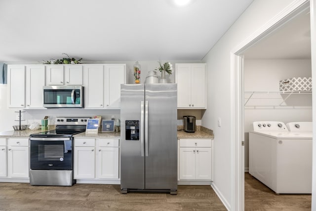 kitchen featuring stainless steel appliances, separate washer and dryer, white cabinetry, light stone countertops, and light hardwood / wood-style flooring