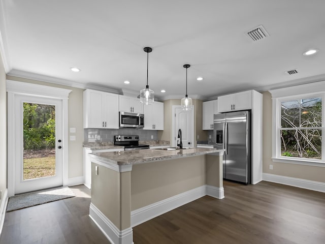 kitchen featuring decorative light fixtures, white cabinetry, a center island with sink, and stainless steel appliances