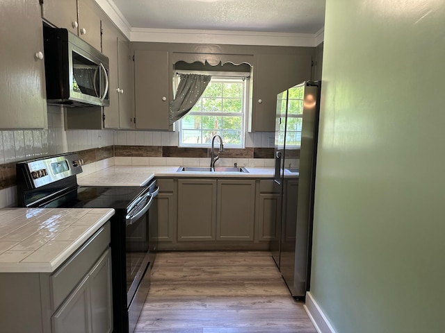 kitchen featuring black range with electric stovetop, stainless steel microwave, a sink, tile counters, and gray cabinets