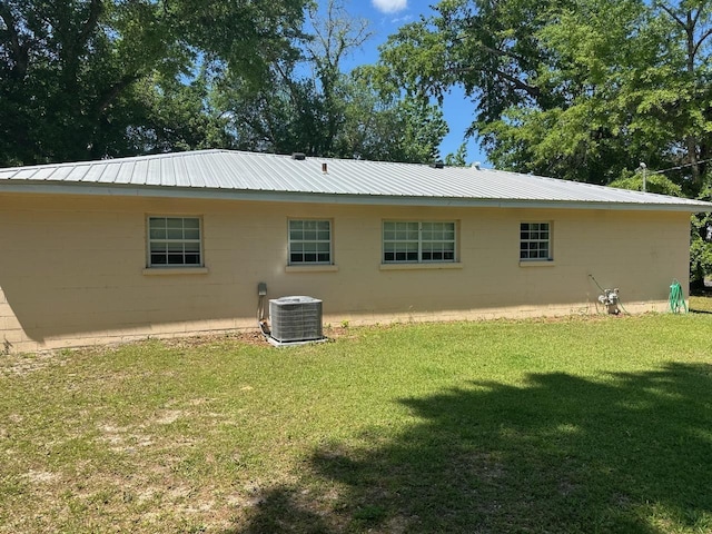rear view of house featuring a yard, metal roof, concrete block siding, and central air condition unit
