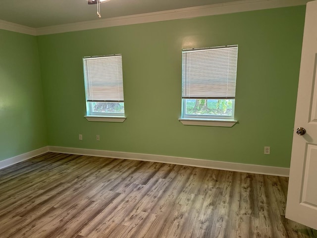 spare room featuring baseboards, ornamental molding, a healthy amount of sunlight, and wood finished floors
