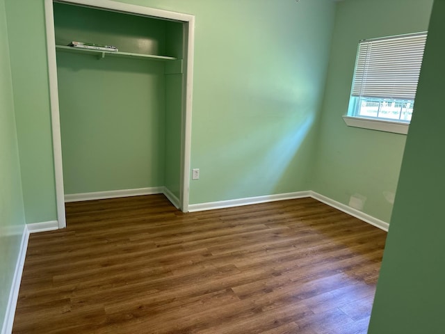 unfurnished bedroom with dark wood-style floors, baseboards, and a closet