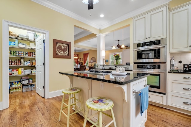 kitchen featuring dark stone counters, decorative backsplash, light hardwood / wood-style flooring, a breakfast bar area, and appliances with stainless steel finishes