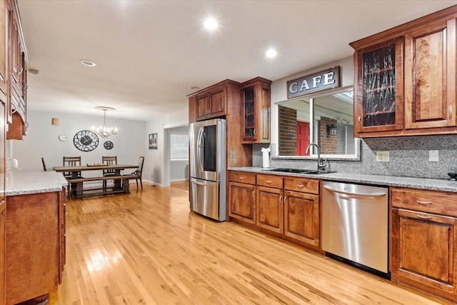 kitchen featuring sink, stainless steel appliances, light stone counters, a chandelier, and light hardwood / wood-style floors