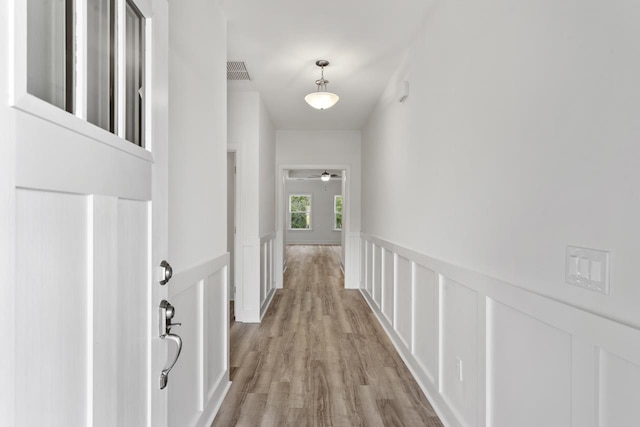 hallway with a wainscoted wall, visible vents, a decorative wall, and light wood finished floors