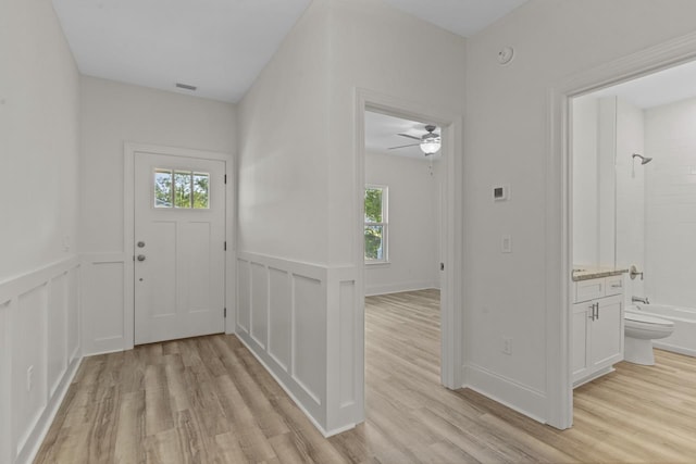 entryway with light wood-type flooring, a wainscoted wall, and a wealth of natural light