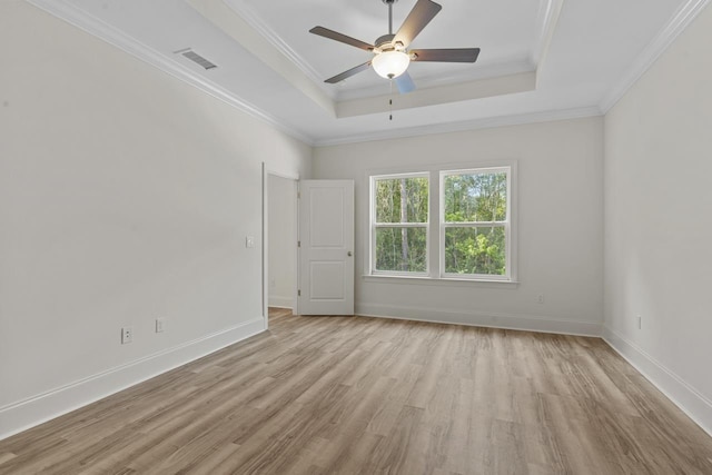 empty room featuring ornamental molding, a tray ceiling, visible vents, and light wood-style floors