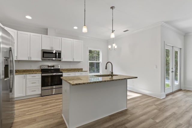 kitchen with stainless steel appliances, an island with sink, a sink, and white cabinetry