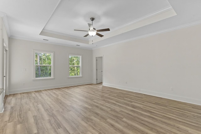 spare room featuring baseboards, ceiling fan, a tray ceiling, crown molding, and light wood-style floors