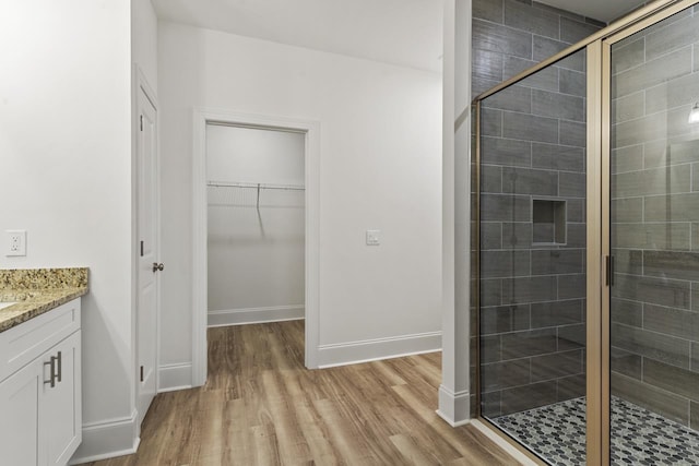 full bathroom featuring wood finished floors, a stall shower, a walk in closet, and vanity