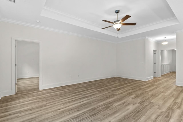 spare room with ornamental molding, light wood finished floors, a raised ceiling, and a ceiling fan