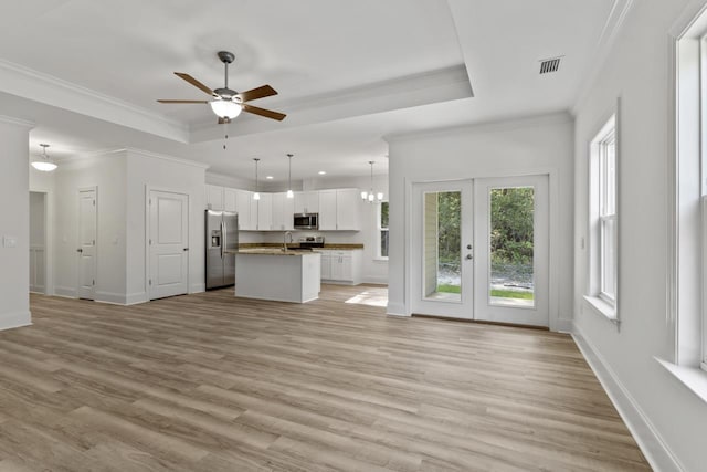 unfurnished living room with a tray ceiling, visible vents, a sink, and light wood finished floors