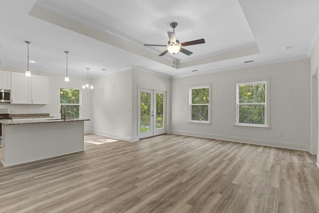 unfurnished living room featuring light wood finished floors, a tray ceiling, ornamental molding, and a wealth of natural light