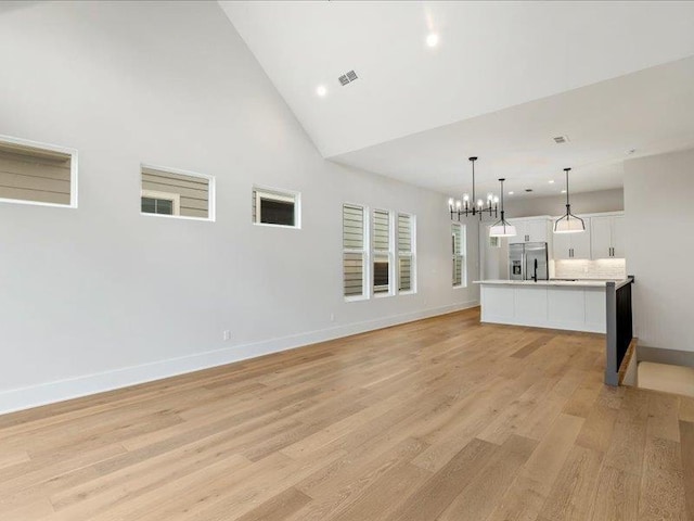 unfurnished living room with light hardwood / wood-style flooring, high vaulted ceiling, and an inviting chandelier