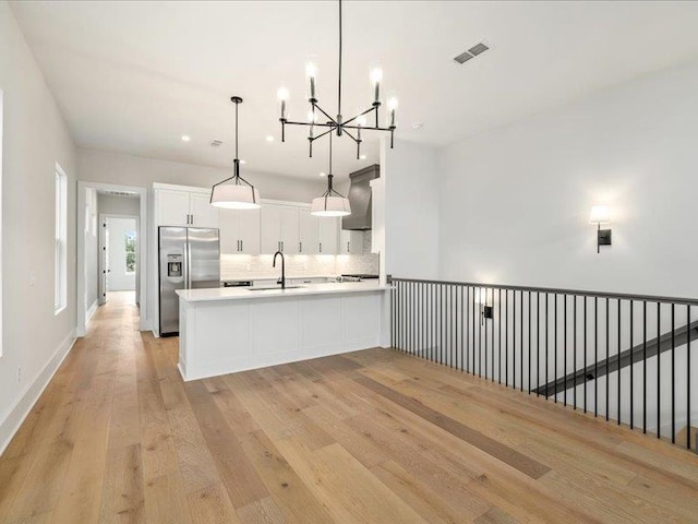 kitchen featuring stainless steel refrigerator with ice dispenser, kitchen peninsula, light wood-type flooring, decorative light fixtures, and white cabinetry