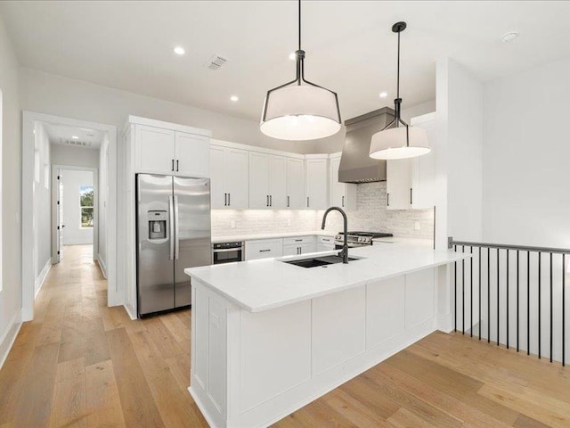 kitchen featuring kitchen peninsula, appliances with stainless steel finishes, premium range hood, sink, and pendant lighting