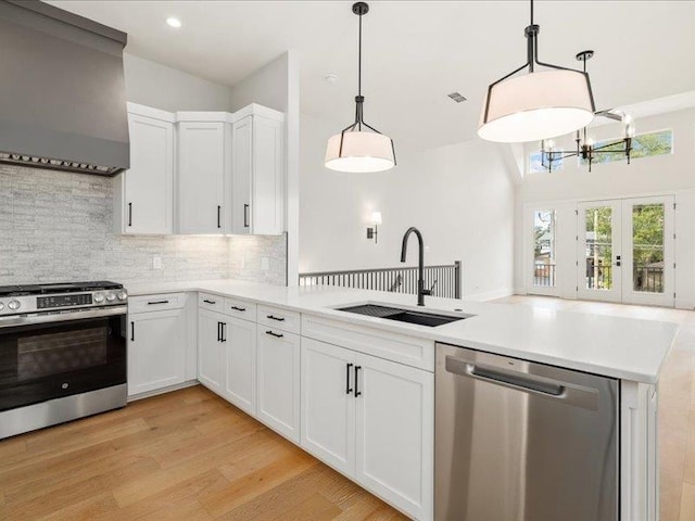 kitchen featuring wall chimney range hood, appliances with stainless steel finishes, decorative light fixtures, light hardwood / wood-style floors, and white cabinetry