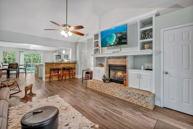 living room with lofted ceiling, hardwood / wood-style floors, built in shelves, and ceiling fan