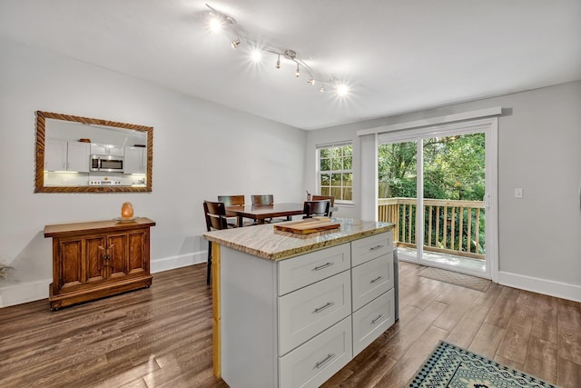 kitchen with white cabinetry, dark wood-type flooring, light stone countertops, and a kitchen island