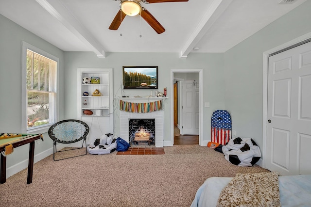 interior space with a brick fireplace, carpet flooring, built in features, beamed ceiling, and ceiling fan