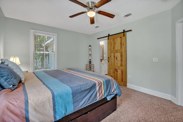 bedroom with ensuite bathroom, a barn door, ceiling fan, and carpet flooring