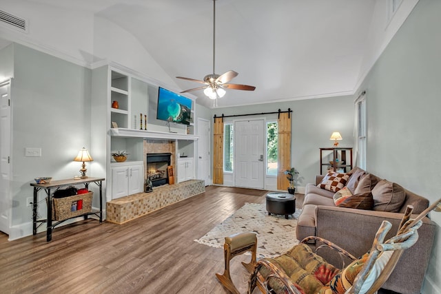 living room with lofted ceiling, ceiling fan, wood-type flooring, built in shelves, and a barn door