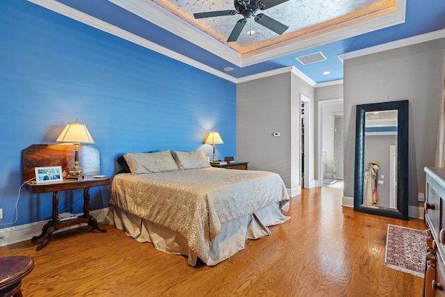 bedroom with crown molding, hardwood / wood-style floors, ceiling fan, and a tray ceiling