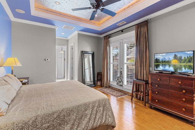 bedroom with crown molding, access to exterior, light hardwood / wood-style floors, and a tray ceiling