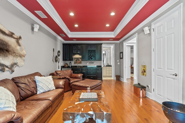 living room featuring hardwood / wood-style flooring, bar area, a tray ceiling, and crown molding