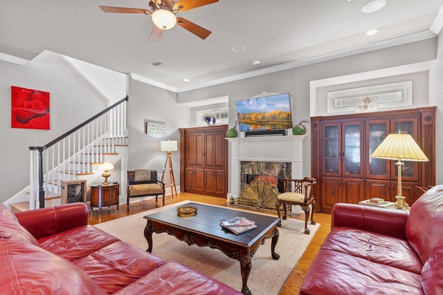 living room with ceiling fan, ornamental molding, a fireplace, and wood-type flooring