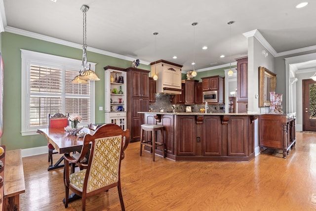 kitchen with stainless steel microwave, decorative light fixtures, tasteful backsplash, a kitchen bar, and light wood-type flooring