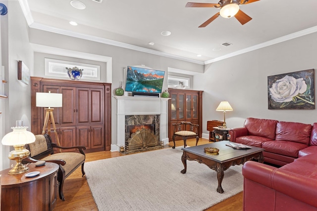 living room with ceiling fan, ornamental molding, a premium fireplace, and light hardwood / wood-style floors