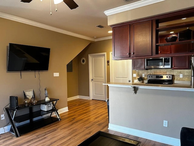 kitchen with a breakfast bar area, tasteful backsplash, light hardwood / wood-style flooring, ornamental molding, and appliances with stainless steel finishes