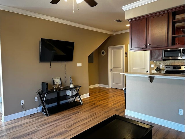 kitchen featuring appliances with stainless steel finishes, a breakfast bar, tasteful backsplash, crown molding, and light wood-type flooring