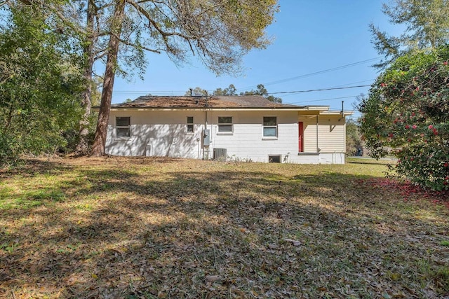 rear view of property with central air condition unit and a lawn