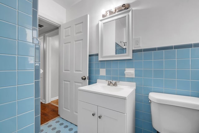 half bath with toilet, wainscoting, tile walls, and vanity