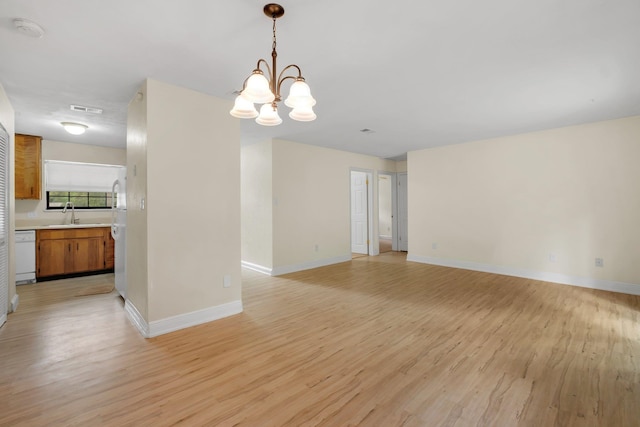 unfurnished room with sink, light wood-type flooring, and an inviting chandelier