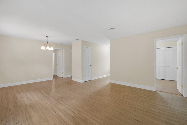 empty room with light hardwood / wood-style flooring and a notable chandelier