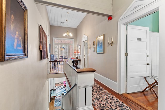 hallway with a chandelier, dark wood-style flooring, baseboards, and an upstairs landing