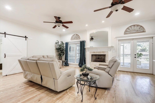 living room with ceiling fan, a barn door, light hardwood / wood-style floors, and french doors