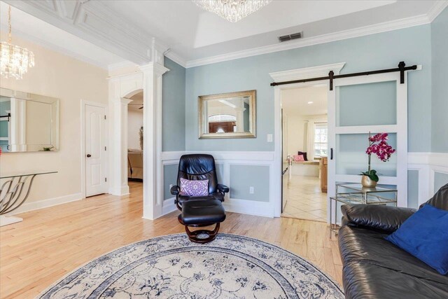 living room featuring a barn door, hardwood / wood-style floors, a notable chandelier, and ornamental molding