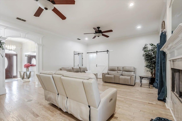 living room with a barn door, crown molding, light hardwood / wood-style flooring, and ceiling fan