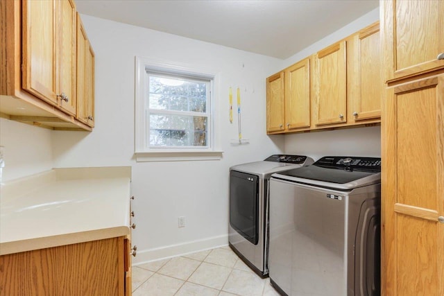 clothes washing area with cabinets, light tile patterned floors, and washing machine and clothes dryer