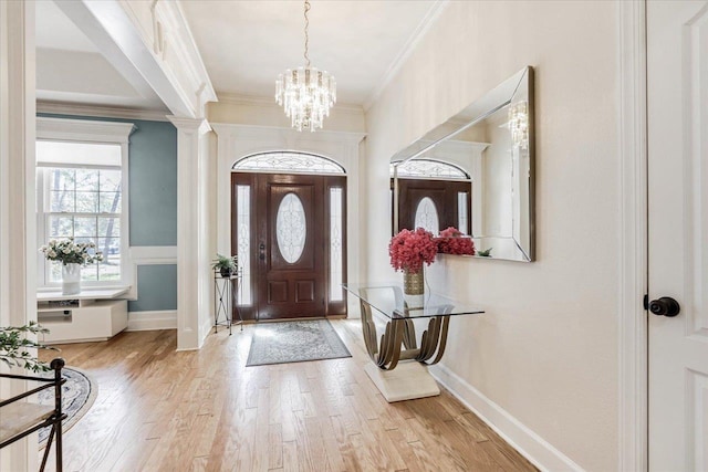 foyer entrance featuring ornate columns, crown molding, a notable chandelier, and light wood-type flooring