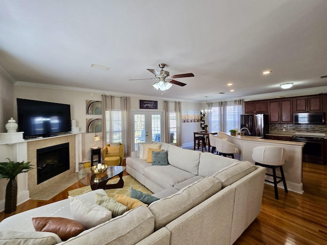 living room featuring a tile fireplace, crown molding, ceiling fan, and wood finished floors